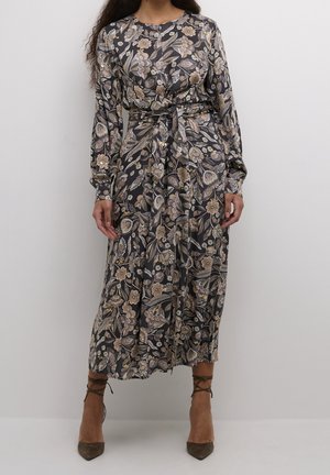 Mujer vistiendo un vestido midi floral de manga larga con cinturón, en tonos suaves, combinado con tacones marrones de punta puntiaguda y cordones.