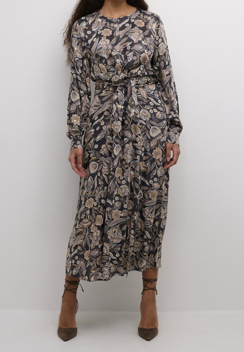 Femme portant une robe midi florale à manches longues avec ceinture, dans des tons doux, associée à des escarpins marron à lacets et bouts pointus.