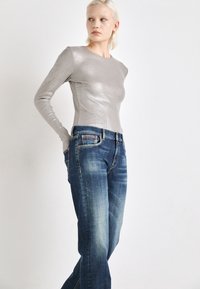 Top plateado de manga larga con una silueta ajustada, combinado con jeans de mezclilla azules con un lavado desgastado y un diseño clásico de cinco bolsillos.