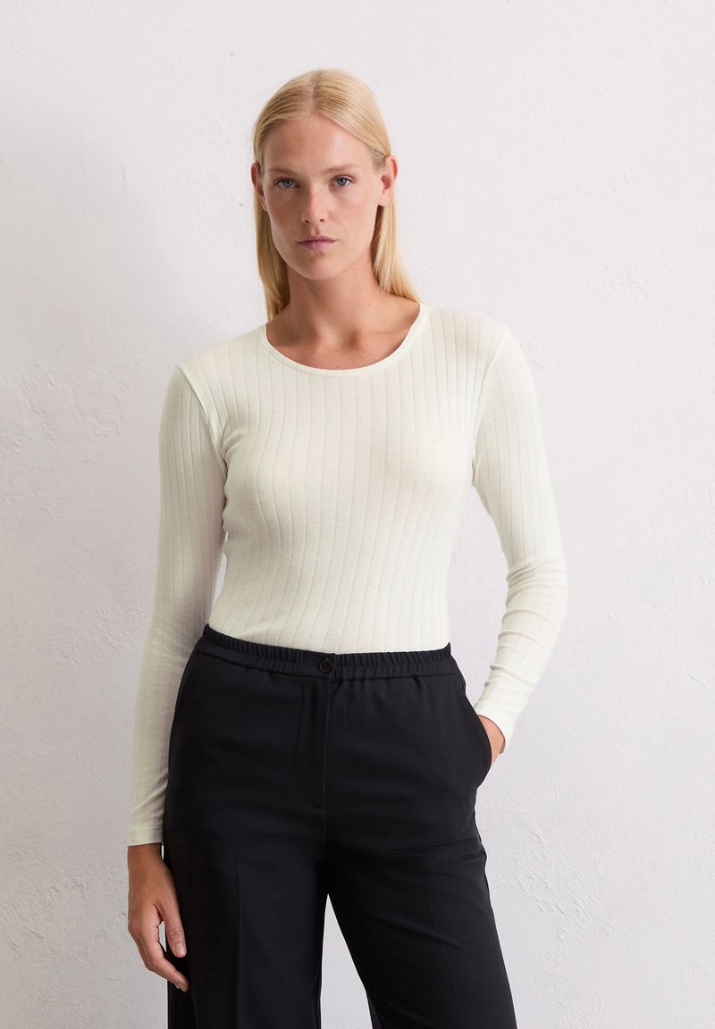 Haut à manches longues côtelé blanc avec un col rond, associé à un pantalon noir ajusté avec une taille élastique et un bouton.