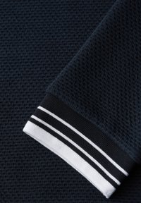 Dunkelblauer strukturierter Stoff mit einem marineblauen Bündchen, das am Rand schwarze und weiße Doppelstreifen aufweist.