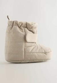Botte en tissu beige doux avec texture matelassée, sangle ajustable, bout rond et semelle en caoutchouc antidérapante. Convient pour un usage intérieur.