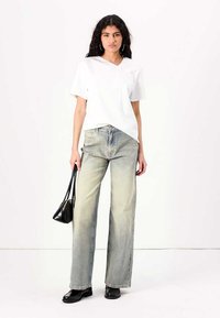 Chemise blanche à manches courtes avec une poche, associée à un jean à jambes larges en délavé clair. Les accessoires comprennent un petit sac à main noir et des chaussures noires.