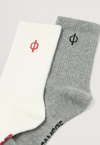 Hvide og grå ribbede sokker med røde og sorte symboler. Den grå sok har tekst på siden, mens den hvide sok har et kontrastlogo.