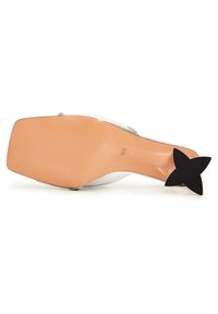 Chaussure à talons hauts blanche avec un bout pointu, featuring un talon en forme d'étoile noir et une semelle lisse couleur beige. Sangle décorative incluse.