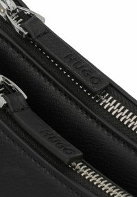 Borsa in pelle nera con doppie zip. Presenta hardware in metallo color argento e tessuto testurizzato con dettaglio del logo embossato sulle linguette delle zip.
