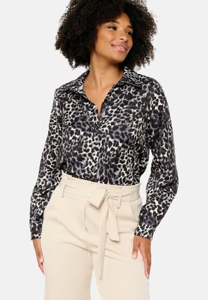 Een blouse met luipaardprint in zwart en crème, met een klassieke kraag en lange mouwen, gecombineerd met hoge beige broeken.