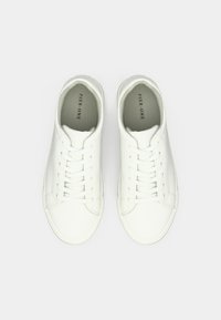 Valge madalate tossude paar kahe paela ja kerge halli „Pier One“ brändingu ning pehmete siseriidega, nähtuna pealt heledal taustal.