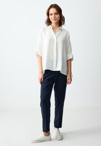 Witte, knoopsluiting shirt met opgerolde mouwen; gecombineerd met marineblauwe, taps toelopende broek en witte sneakers. Gladde, lichte stof met een relaxte pasvorm.