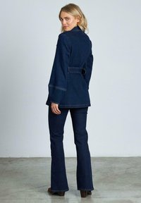 Giacca di jeans scura con vita a cintura, jeans svasati e maniche lunghe. Presenta cuciture visibili e un design semplice in silhouette aderente.