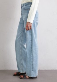 Lichtblauwe, wijde jeans met een hoge taille, met subtiele vervaging, vijf-pocketdesign en een rechte snit. Gedragen met zwarte sandalen.