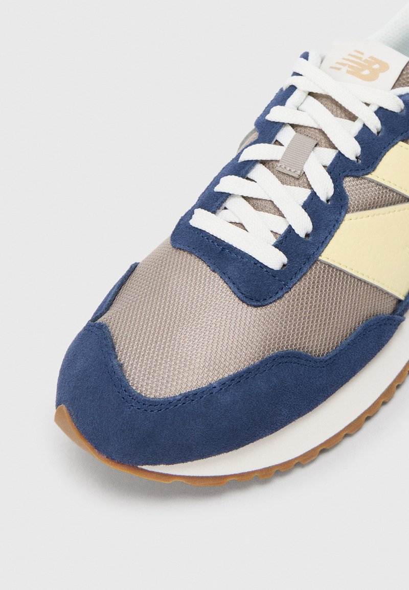 Marineblauwe en tan sneaker met mesh en suède materialen, voorzien van witte veters, een gestructureerde bovenkant en een tan rubberen zool.