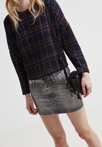 Námořnicky modré a červené kostkované tričko s dlouhým rukávem a volným střihem, spárované s vybledlou šedou denimovou minisukní a malou černou kabelkou přes rameno.