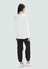 Weißer gestrickter Pullover mit rundem Halsausschnitt und geripptem Saum, kombiniert mit schwarzen elastischen Hosen mit Bündchen und weißen Sneakers.