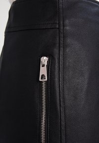 Musta nahkahame, jossa on hopeinen vetoketj yksityiskohta sivussa, teksturoitu pinta ja sileät saumat, suunniteltu tiukaksi malliksi.