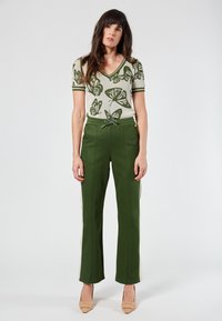Green trousers with side stripes and a drawstring waist, paired with a cream V-neck top featuring a green butterfly pattern.