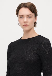Czarna bluzka z długim rękawem, z teksturowanym kwiatowym wzorem, okrągłym dekoltem i dopasowanym krojem. Gładki materiał o lekkiej przezroczystości.