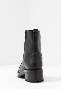 Zwarte leren enkellaars met een ronde neus, een gestructureerde afwerking en een lage blokhak. Voorzien van een rits aan de achterkant.
