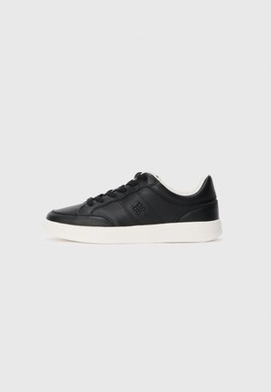 Black low-top leather sneaker with black laces, white sole, and subtle embossed logo on the side, shown from the outer side.
