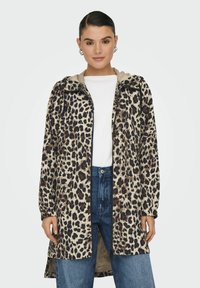 Giacca con stampa leopardata e interno beige, con zip frontale e polsini elasticizzati, abbinata a jeans blu a vita alta e una maglietta bianca.