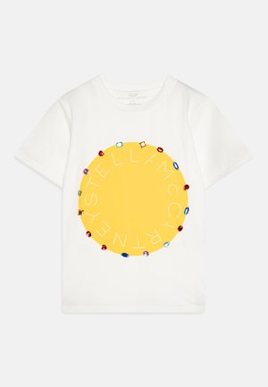 Hvit bomulls t-skjorte med en stor gul sirkel med juvel-lignende detaljer. Teksten "STELLA McCARTNEY" er arrangert rundt sirkelen.
