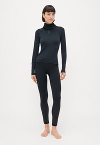 Maglietta sportiva nera a maniche lunghe con colletto alto e leggings neri attillati con dettagli texturizzati alle caviglie. Tessuto elastico e liscio.