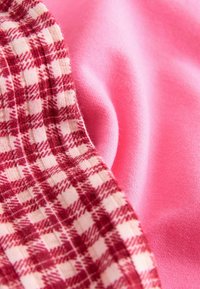 Primo piano di un tessuto rosa con texture morbida accanto a un tessuto a quadri rosso e bianco con cuciture visibili.