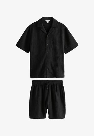 Fekete, texturált rövid ujjú gombos ing gallérral, hozzá illő, megkötős rövidnadrággal, fehér háttéren laposan elhelyezve.