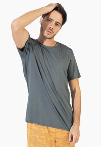 Camiseta gris de manga corta con cuello redondo, fabricada con un tejido texturizado y un logo sutil. Se lleva con pantalones cortos de patrón naranja claro.