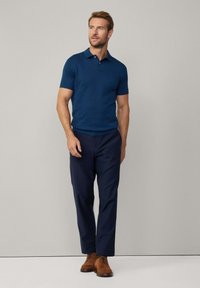 Mörkblå polo shirt med korta ärmar, i kombination med mörkblå byxor och bruna mockaskor; enkel design med klassisk passform.