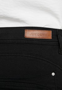 Svarta denimjeans med en läderlapp märkt "JDY DENIM." Har silverdetaljer och klassiska sömmar. Justerbart midjeband.