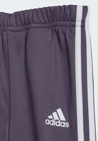 Pantaloni sportivi viola con tessuto testurizzato. Presentano una vita elastica e strisce bianche ai lati. Comprendono un piccolo logo Adidas bianco.