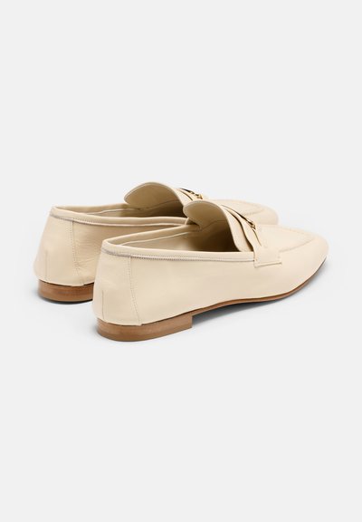 Mocassins en cuir crème avec une semelle en bois plate. Présentent un design plié à l'avant et une couture subtile le long des bords. Pas de matériel proéminent.