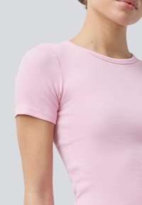 Kurzärmliges, geripptes T-Shirt in Hellrosa, mit Rundhalsausschnitt und taillierter Silhouette. Glatte Textur und saubere Nähte.