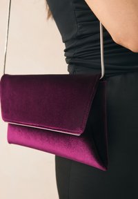 Pochette en velours violet avec un design élégant à rabat et une chaîne argentée, présentant une texture lisse et une silhouette élégante.
