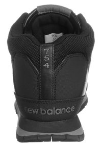 Chaussure de sport noire avec tige en mesh, col rembourré, semelle en caoutchouc et marquage "new balance". Numéro de modèle 754 embossé sur le talon.