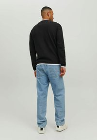 Felpa nera in cotone con collo a giro e jeans di denim blu chiaro. Sneakers bianche con un'accentuazione nera sul tallone. Design semplice e casual.