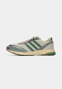 Scarpa sportiva low-top con upper in mesh beige, strisce verdi, lacci beige e suola beige con accenti verdi e marroni.