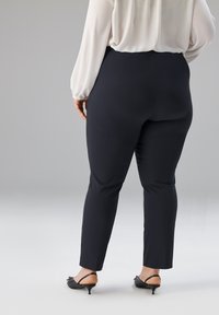 Dunkelblaue Hosen in Slim-Fit-Design, hergestellt aus glattem Stoff mit mittlerer Taillenhöhe, kombiniert mit schwarzem Schuhwerk mit kleinem Absatz.