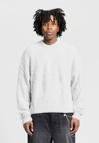 White, fluffy sweater with a ribbed neckline and cuffs. Features a loose fit and textured fabric, paired with dark, loose-fitting pants.
