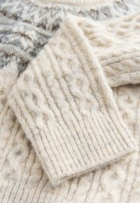 Cable-knit cream sweater featuring a textured pattern, ribbed cuffs, and a soft, fuzzy finish with subtle grey and brown accents.
