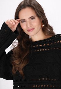 Maglione nero lavorato a maglia con un design testurizzato caratterizzato da trecce e sezioni a giorno. Le maniche sono ampie e lo scollo è rotondo.