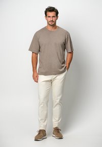 Brązowa bawełniana koszulka z krótkim rękawem w połączeniu z białymi spodniami i brązowymi sneakersami. Minimalistyczny design, luźny krój i neutralna kolorystyka.