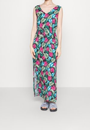 Robe maxi sans manches à col en V avec motif de feuilles tropicales colorées en rose, bleu et vert, portée avec des sandales légères bleu clair sans lacets.