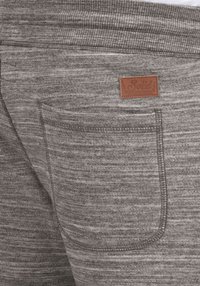 Le pantalon de survêtement gris présente un motif texturé chiné avec une taille élastique et une étiquette en cuir brun cousue sur la poche arrière.