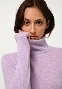 Maglione a collo alto di colore viola chiaro, realizzato in un tessuto morbido e texturizzato. Presenta maniche lunghe con polsini a coste e un design del colletto aderente.
