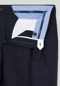 Pantaloni blu scuro con una texture liscia, dotati di chiusura con zip, dettagli bianchi e una cintura interna a righe blu.