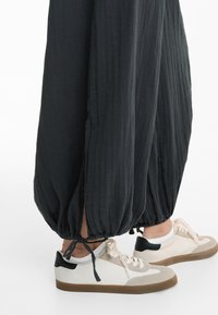 Črne, ohlapne hlače z nabranimi gležnji in stranskimi razporki; v kombinaciji z nizkimi teniskami v krem in bež barvi z črnimi akcenti.