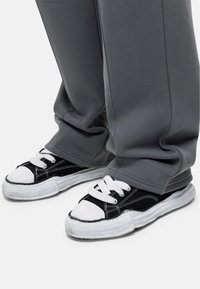 Zwart-witte sneakers met een canvas bovenkant, rubberen zool en witte veters, gecombineerd met grijze sweatpants met een ontspannen pasvorm.