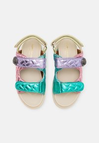 Kleurige sandalen hebben metallic roze, paarse en teal banden met klittenbandsluitingen, een geborduurde textuur en een decoratieve hardwareaccent.